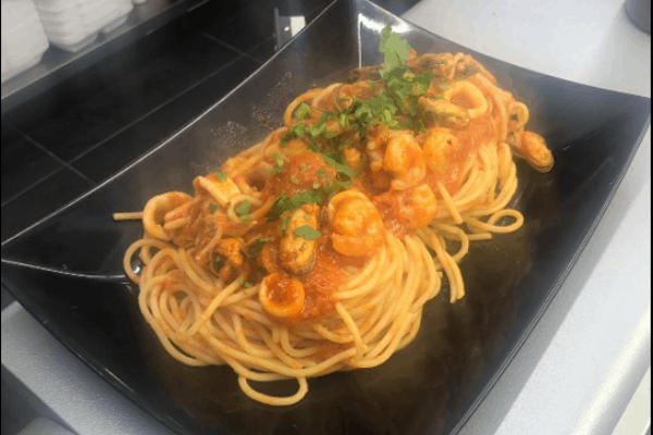 A dish of spaghetti with seafood sauce from Maurizio's SQ is on a black plate.